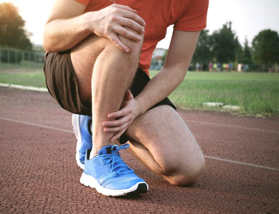 An athlete holds their knee and shin as if they are experiencing leg pain